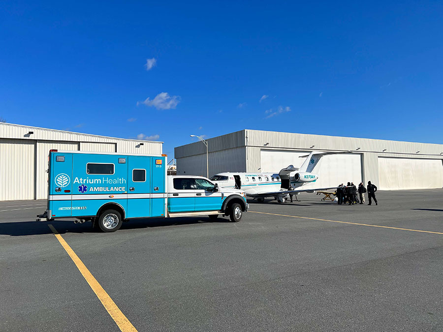 A teal ambulance sitting next to an airplane on an airport tarmac.