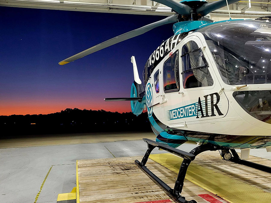 A teal, blue and white helicopter parked on a helipad.