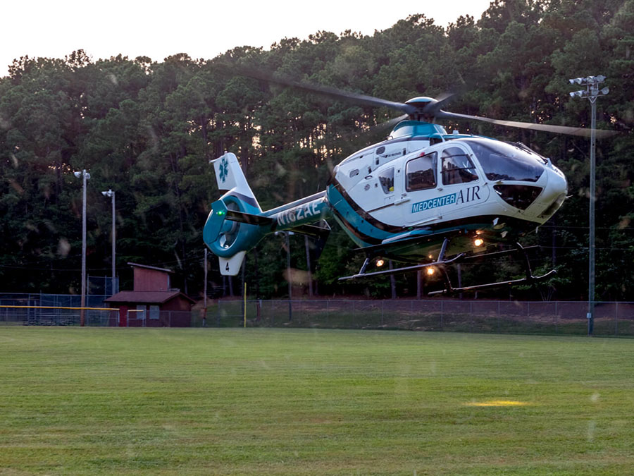 A teal, blue and white helicopter in flight about to land in a grassy field.
