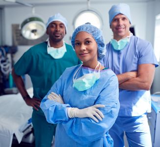 Woman and men in scrubs smiling with arms crossed in operating room.