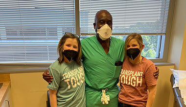 Twins in blue and pink shirts pose for a photo with their doctor. All three are wearing masks.