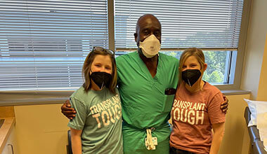 Twins in blue and pink shirts pose for a photo with their doctor. All three are wearing masks.
