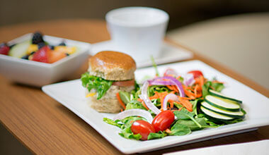 A table with two plates of vegetables and a sandwich next to a white cup.