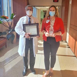 Derek Raghavan, MD, president of Atrium Health Levine Cancer Institute poses with Laura and the Planetree award, honoring LCI