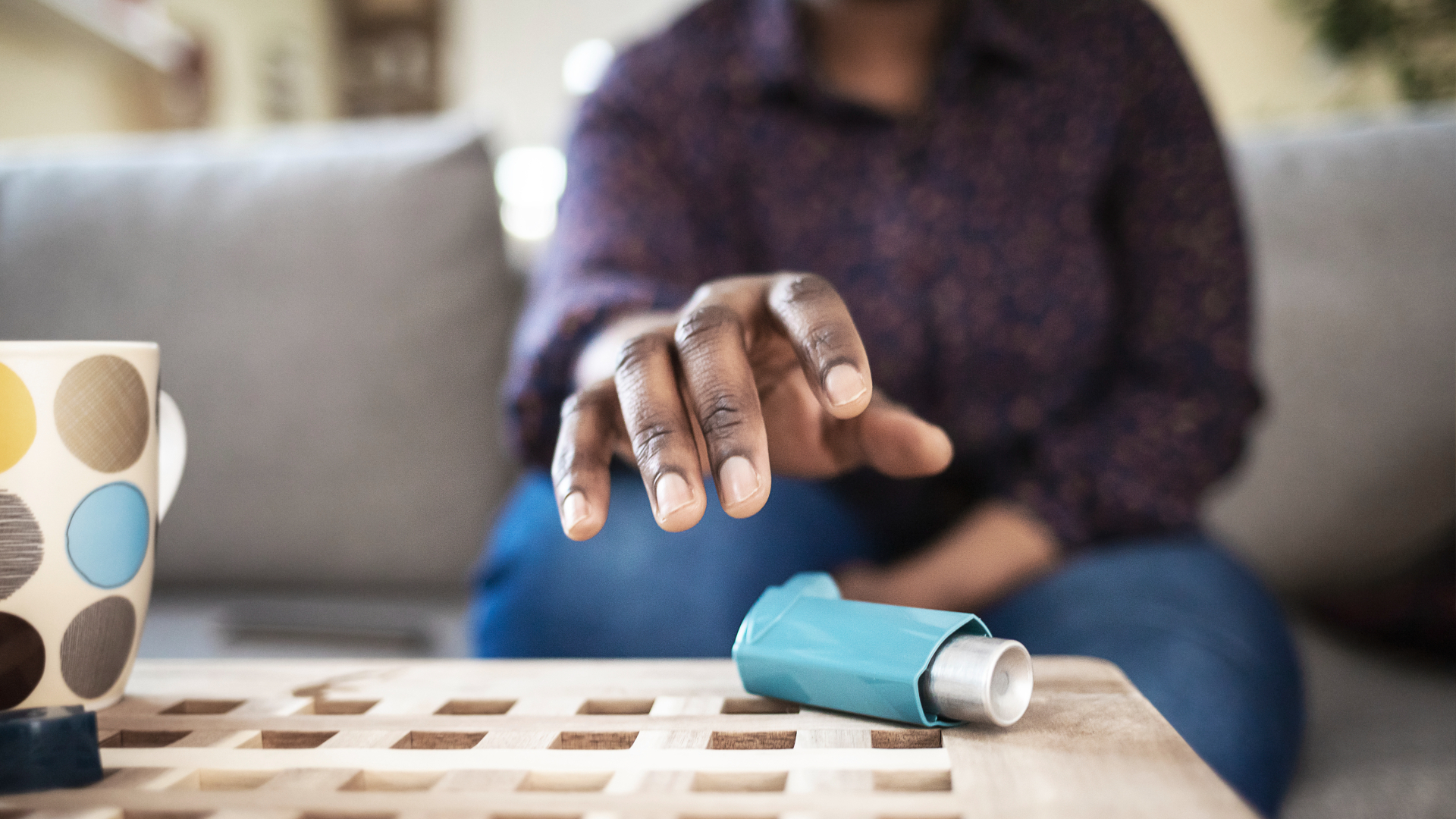 An African-American woman reaches for her inhaler on her coffee table