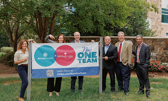 A group of men and women standing together outside next to an outdoor banner.