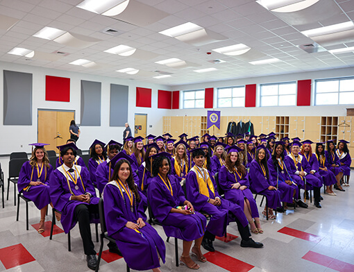 A group of early college students sitting at their graduation in their caps and gowns.