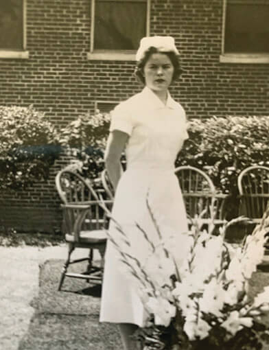 A nurse in a white hat and outfit standing in a courtyard.