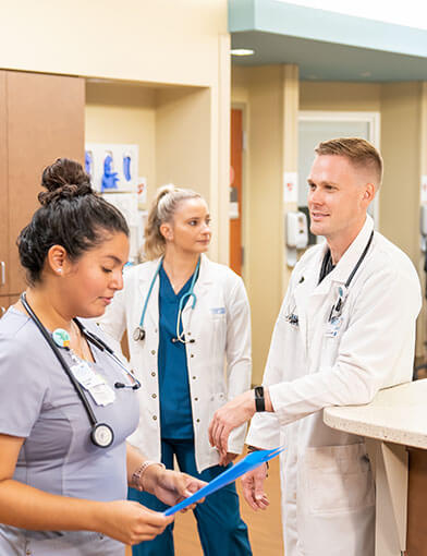 Three doctors, one male and two female, talking in a hallway.