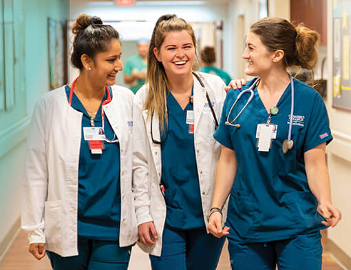 A group of nurses in blue scrubs walking down a hallway.