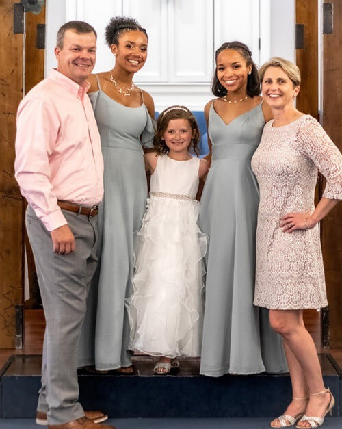 A family of five standing side by side and smiling at the camera.