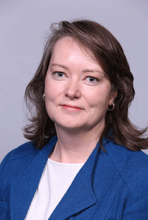 A woman with long brown hair, wearing a blue blazer and looking at the camera.