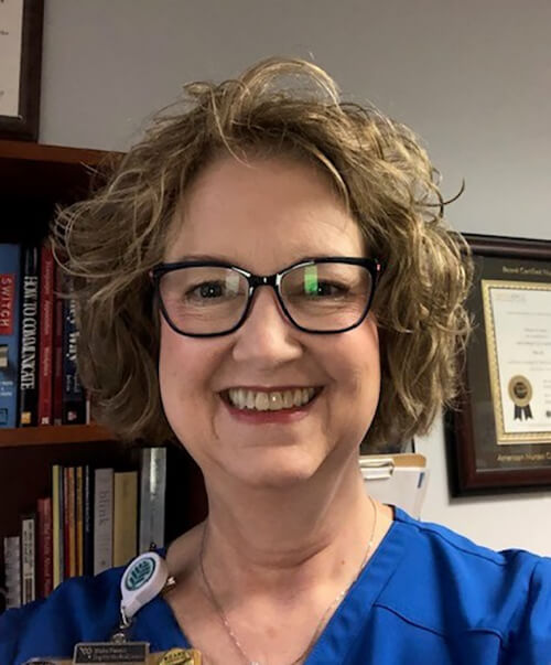 A woman with short hair wearing a blue shirt and smiling at the camera.