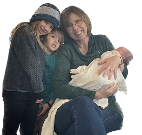 A woman holding a baby while kneeling beside two small children and smiling at the camera.