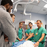 Four medical students gathered around a teacher looking at a medical gurney.