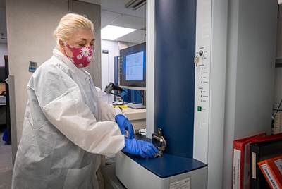 Woman in protective lab gear wearing mask operating machine