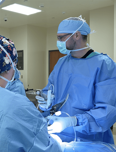 Surgeons in blue scrubs and gear performing a surgery.