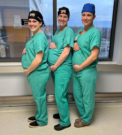 Three pregnant medical professionals wearing scrubs and smiling at the camera.