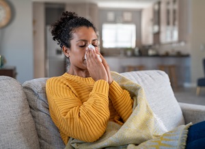 Woman at home on the couch blowing her nose