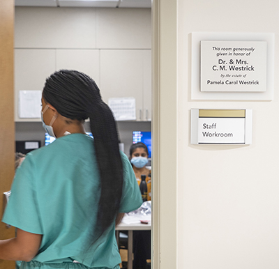 African-American woman in green scrubs walks through door with signs on wall to right of door