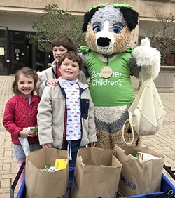 Brenn, one of the Brenner Children’s mascots, stands with some of the children who helped bring in food and funds for the pediatric food bank at the Downtown Health Plaza in February.