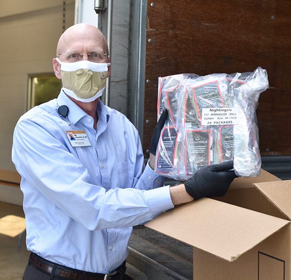 Bald man wearing facial mask holds up a plastic bag full of same kind of masks