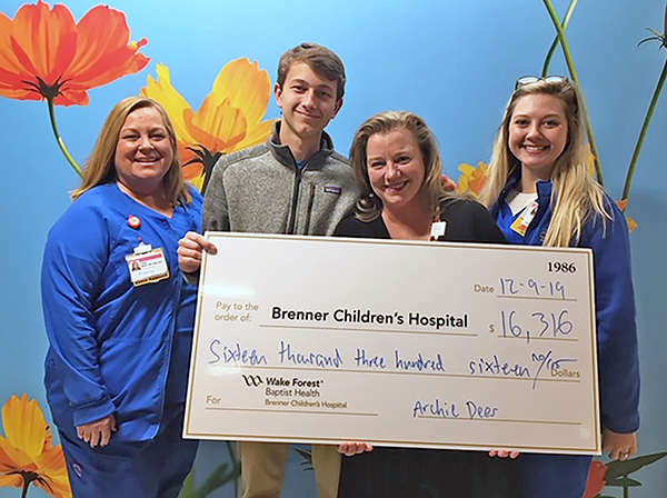 A male teen and three women smile at the camera and pose with a charity check