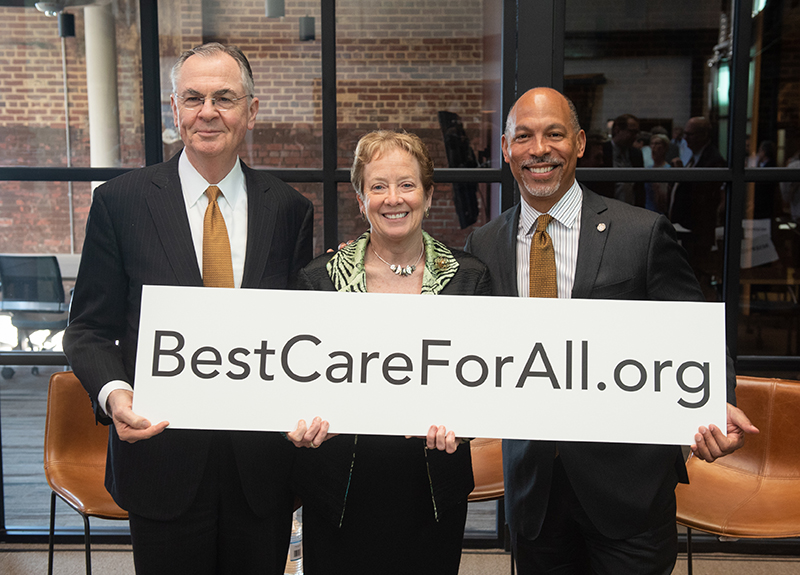 A Caucasian man, Caucasian woman and African American man stand holding a sign reading 'BestCareForAll.org'