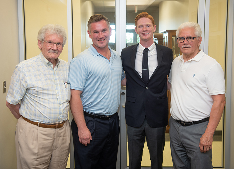 Four men of varying ages from the Crouse family stand in front of sliding doors in a yellow hallway