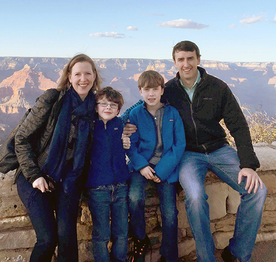 A mother, father and two children sitting on a bench in front of the Grand Canyon