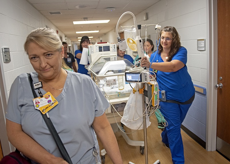 Nurses and medical staff move an isolette down a hall