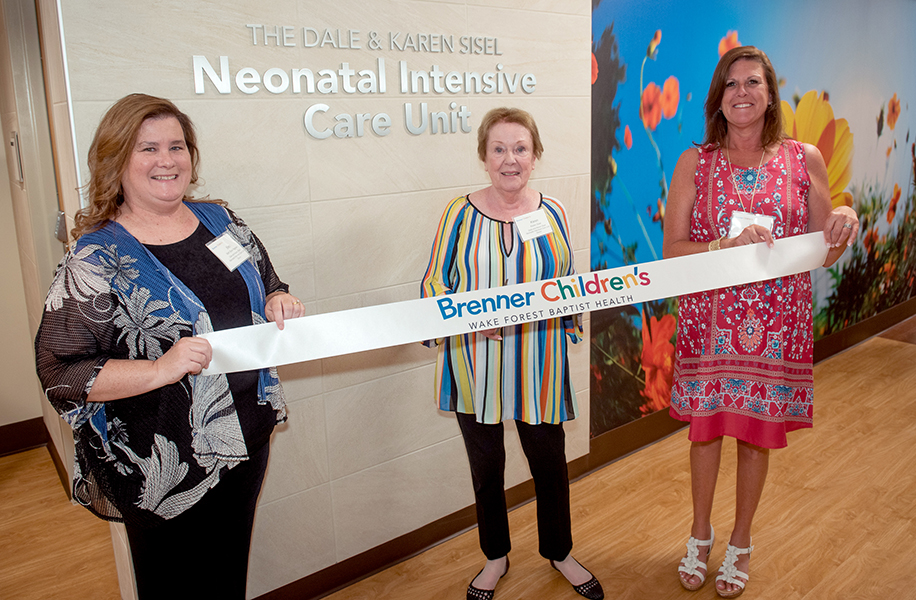 Karen Sisel stands in the middle of a ribbon at the opening of the Dale and Karen Sisel NICU with her daughters, Beth Sisel Agejew and Paige Sisel Bowles.