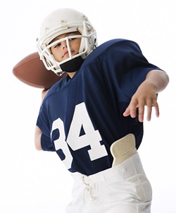 Stock photo of youth football player in navy jersey and white pants, throwing a football