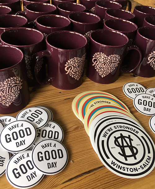 Burgundy mugs with 'resilience' in a heart, Winston-Salem stickers and coasters