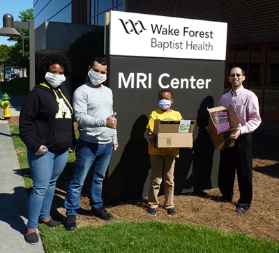 Three adults and one child, all of whom wear masks, stand in front of the MRI Center sign