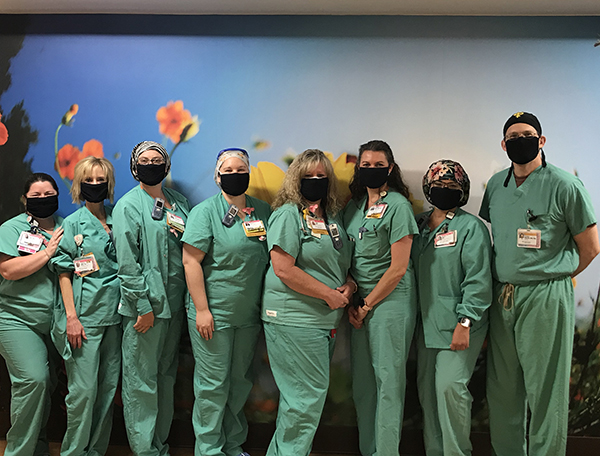 A group of nurses in green scrubs and masks stands in front of a mural of large wildflowers