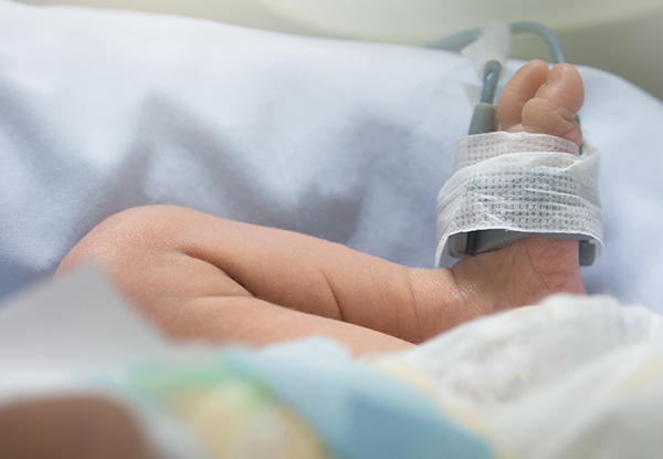 Newborn baby feet and leg with oxygen saturation monitor or pulse oximeter machine, lying in incubator