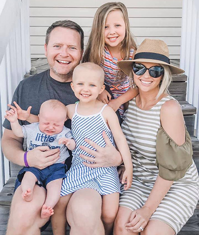 Caucasian family (father, mother, two daughters and a baby) pose and smile for a group picture in summer