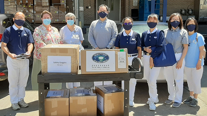 A group of adults stands behind and beside a rolling cart carrying boxes of PPE