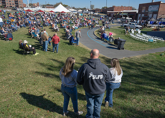 Two women and one man stand on a hill overlooking a large crowd of people.