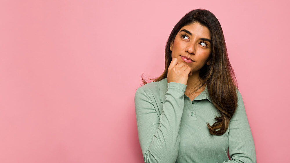 A woman standing in front of a pink background.