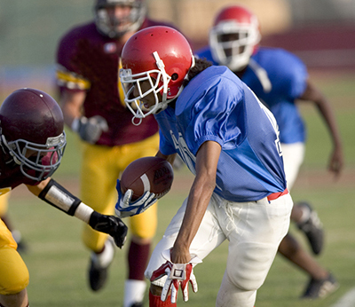 Boy in blue and white football uniform with red helmet evades tackle