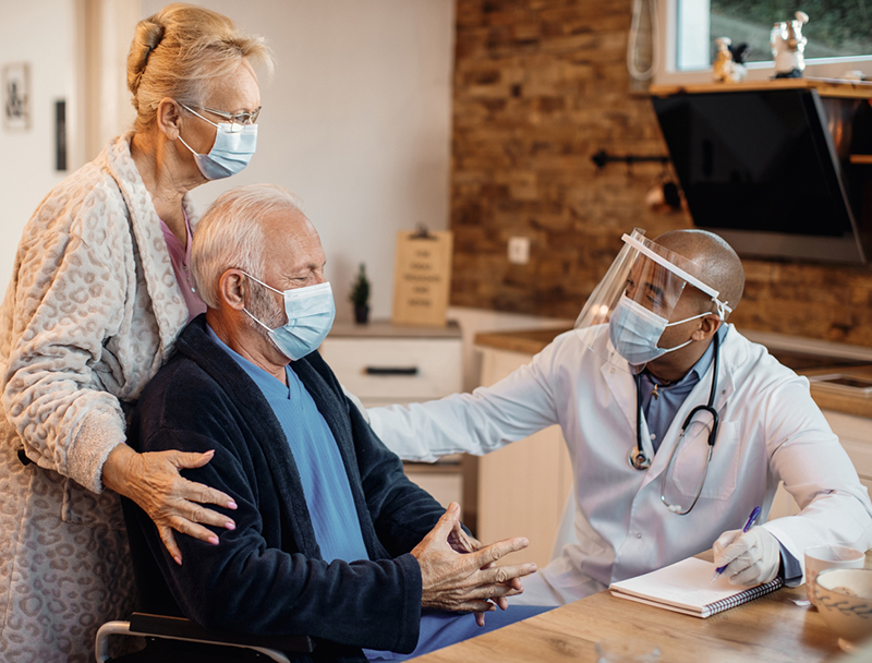 Mature couple and black doctor wearing protective face masks while talking at home.