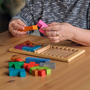 Elderly woman sitting at table and sorting spatial puzzle pieces