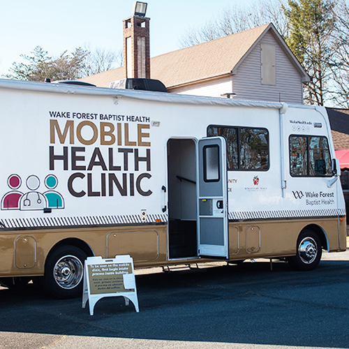Gold and white RV in parking lot; "Mobile Health Clinic" painted on the side