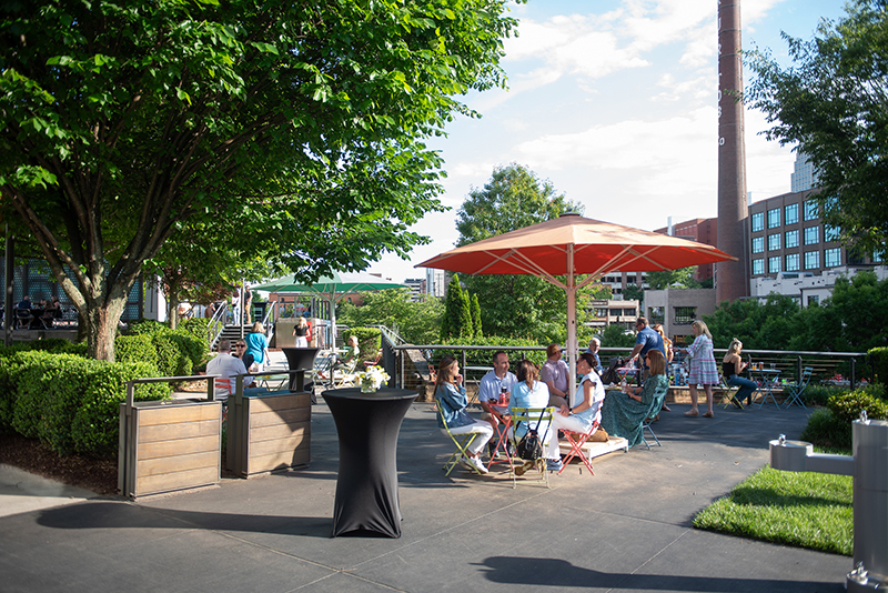 A group of people gathered under a red awning while surrounded by trees.
