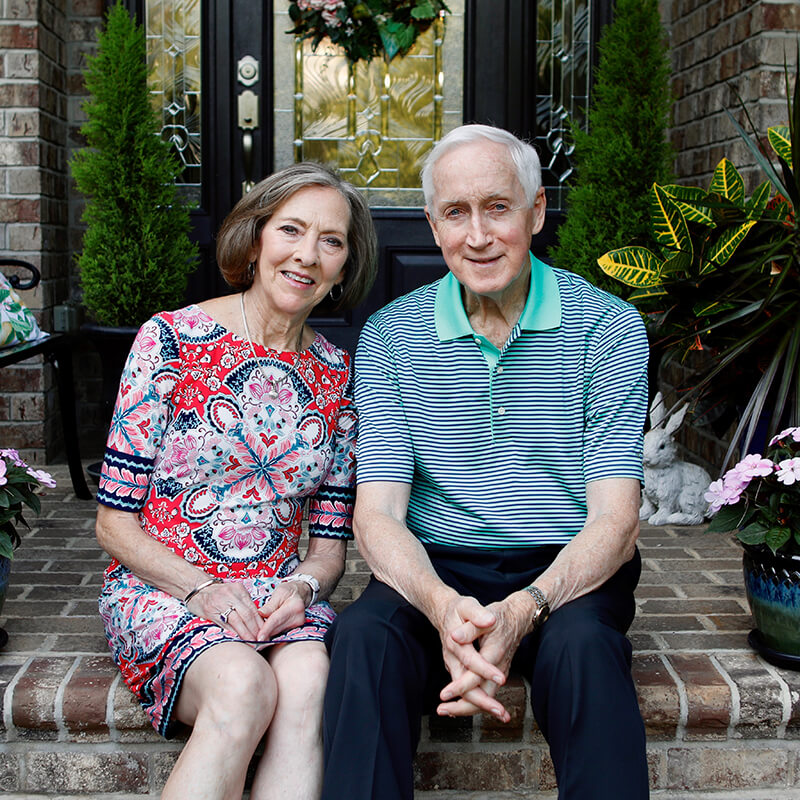 A couple sitting on the steps of a porch smiling at the camera.