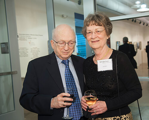 An older man and woman standing side-by-side and smiling at the camera.