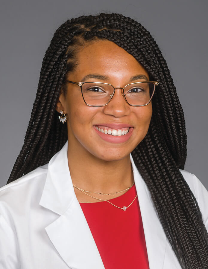 A medical student wearing a lab coat smiling at the camera.