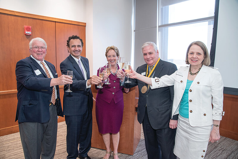 Five men and women standing side-by-side holding up champagne glasses.